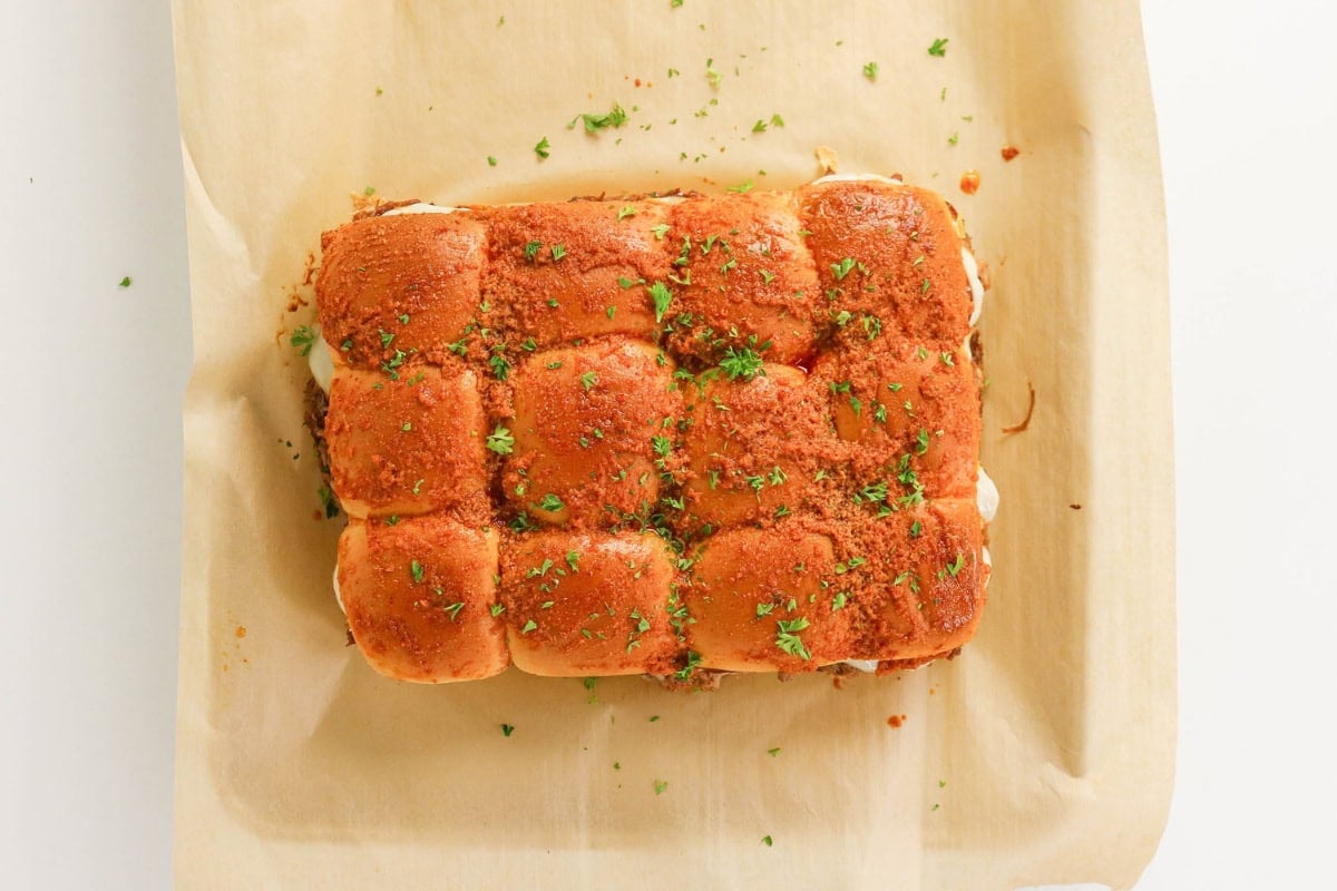 Nine slider sandwiches topped with herbs on parchment paper.