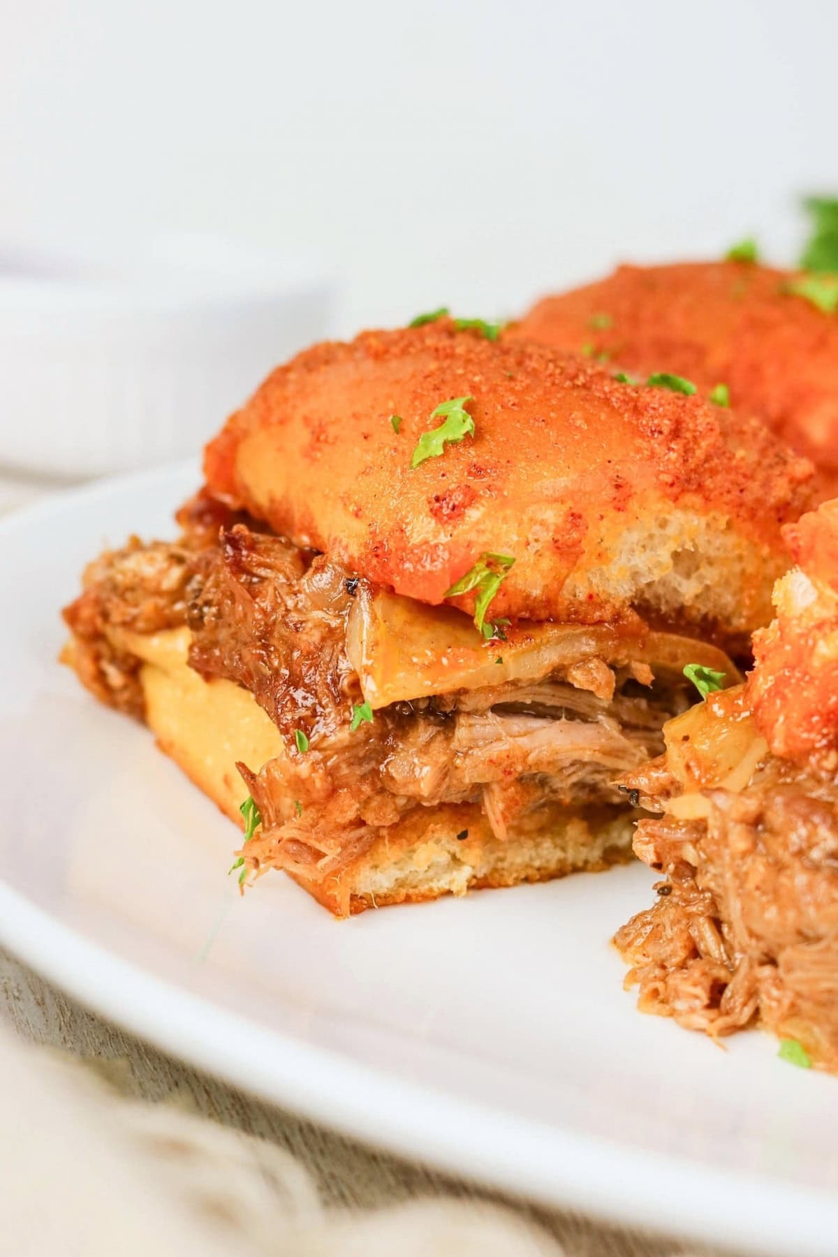 Close-up of a pulled beef sandwich with melted cheese on a white plate.