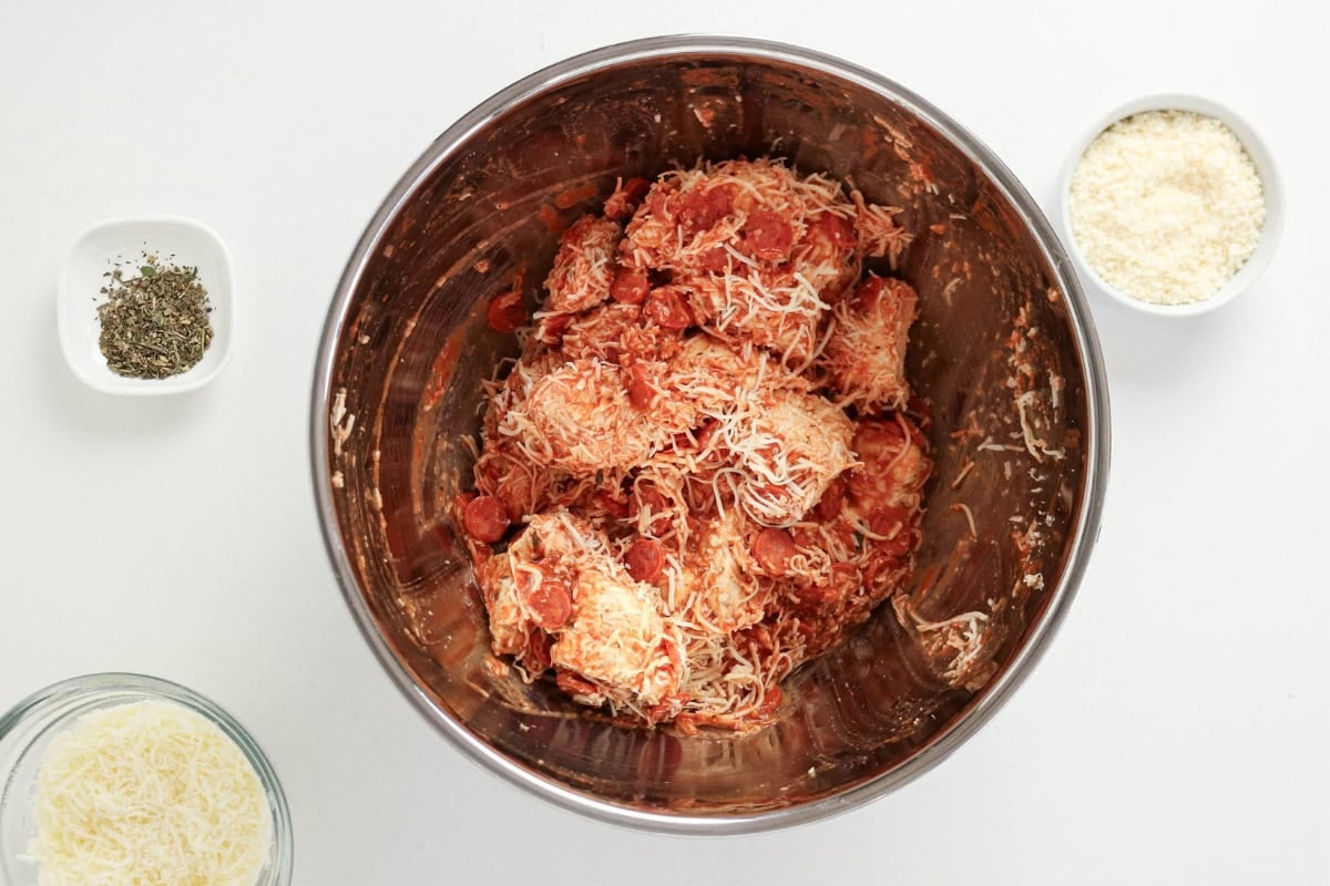 Dough balls mixed with pepperoni and cheese in a metal bowl, with side toppings.