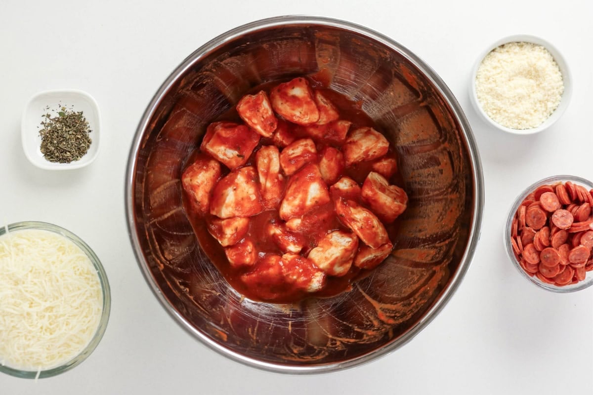 Chunks of chicken in red sauce surrounded by bowls of cheese, herbs, and meat.