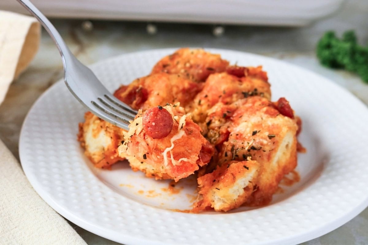 A fork lifting a piece of pizza-style monkey bread from a white plate.