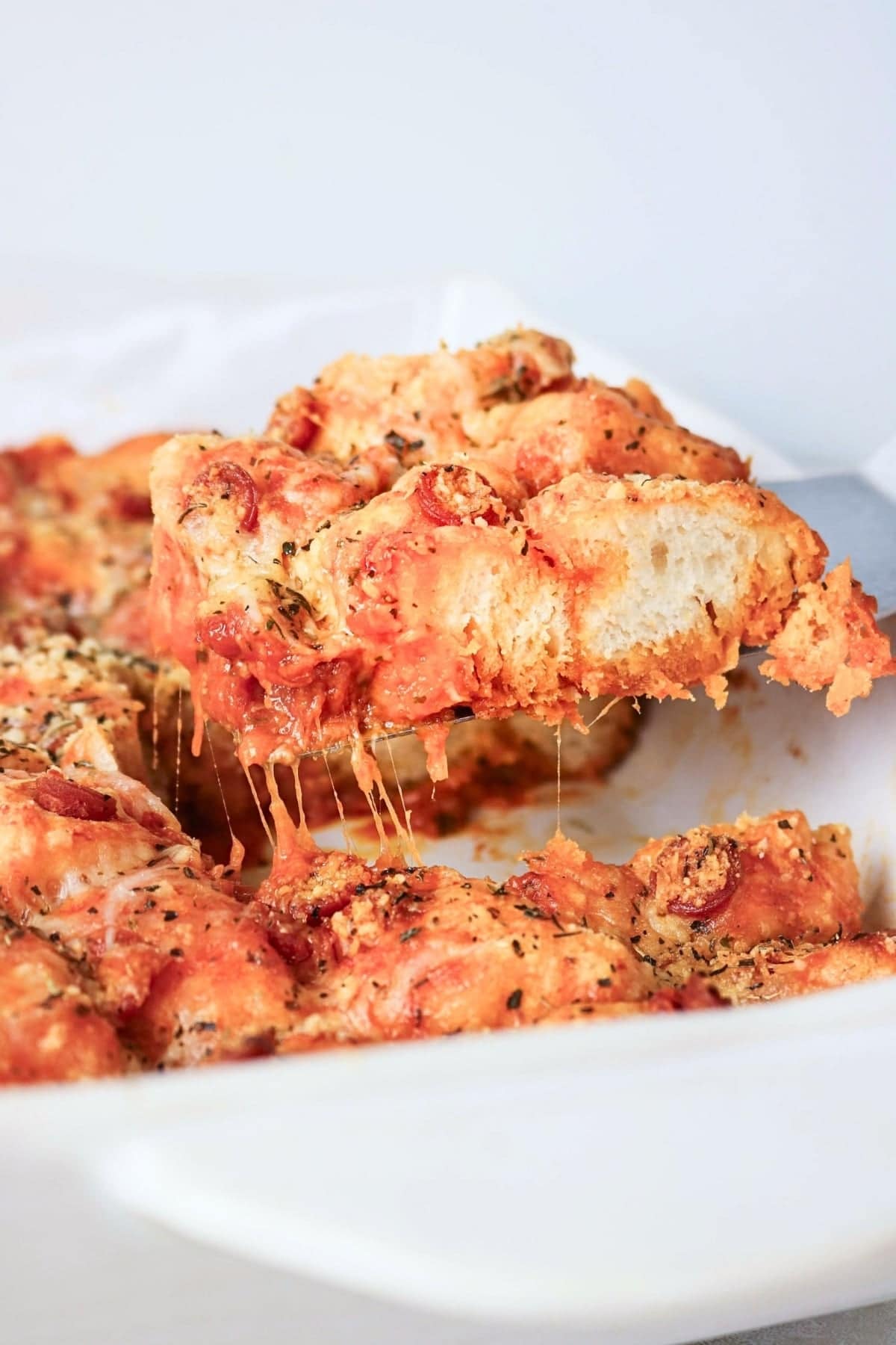 A serving of pizza monkey bread being lifted from a baking dish.
