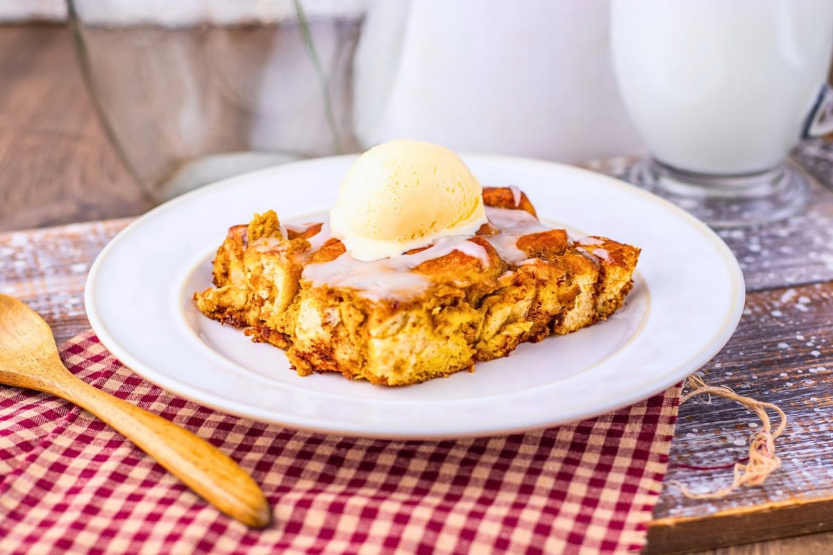 A square of bread pudding topped with a scoop of vanilla ice cream.