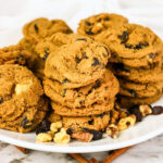 A plate of oatmeal raisin cookies with scattered walnuts and raisins.