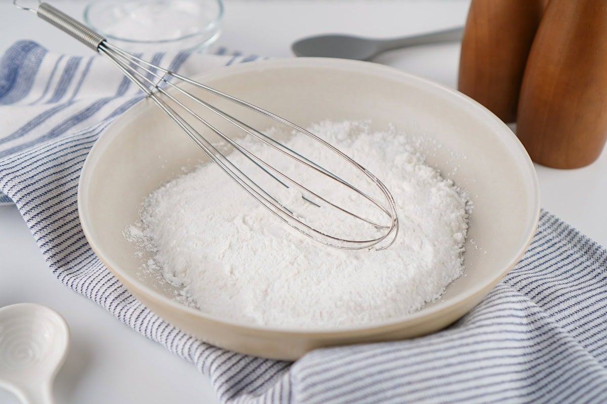 A wire whisk resting in a bowl of white powder.