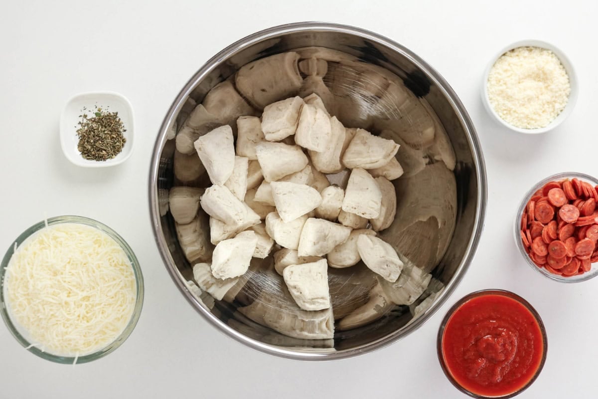 Metal bowl of raw dough chunks surrounded by small bowls of pizza ingredients.