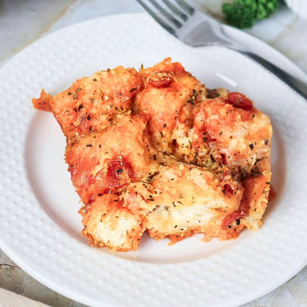 A serving of cheesy pull-apart pizza bread on a white plate with a fork.