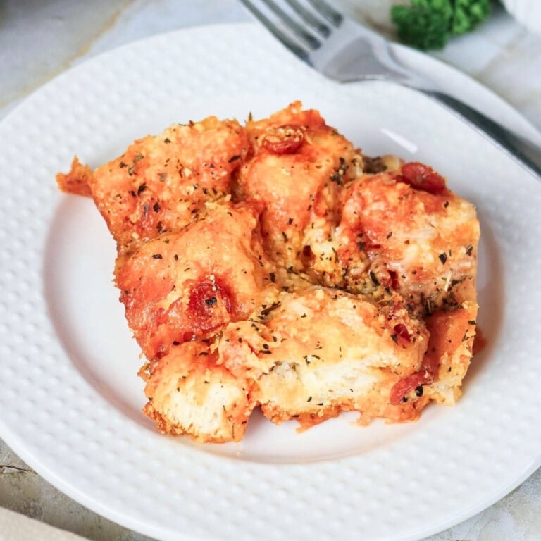 A serving of cheesy pull-apart pizza bread on a white plate with a fork.