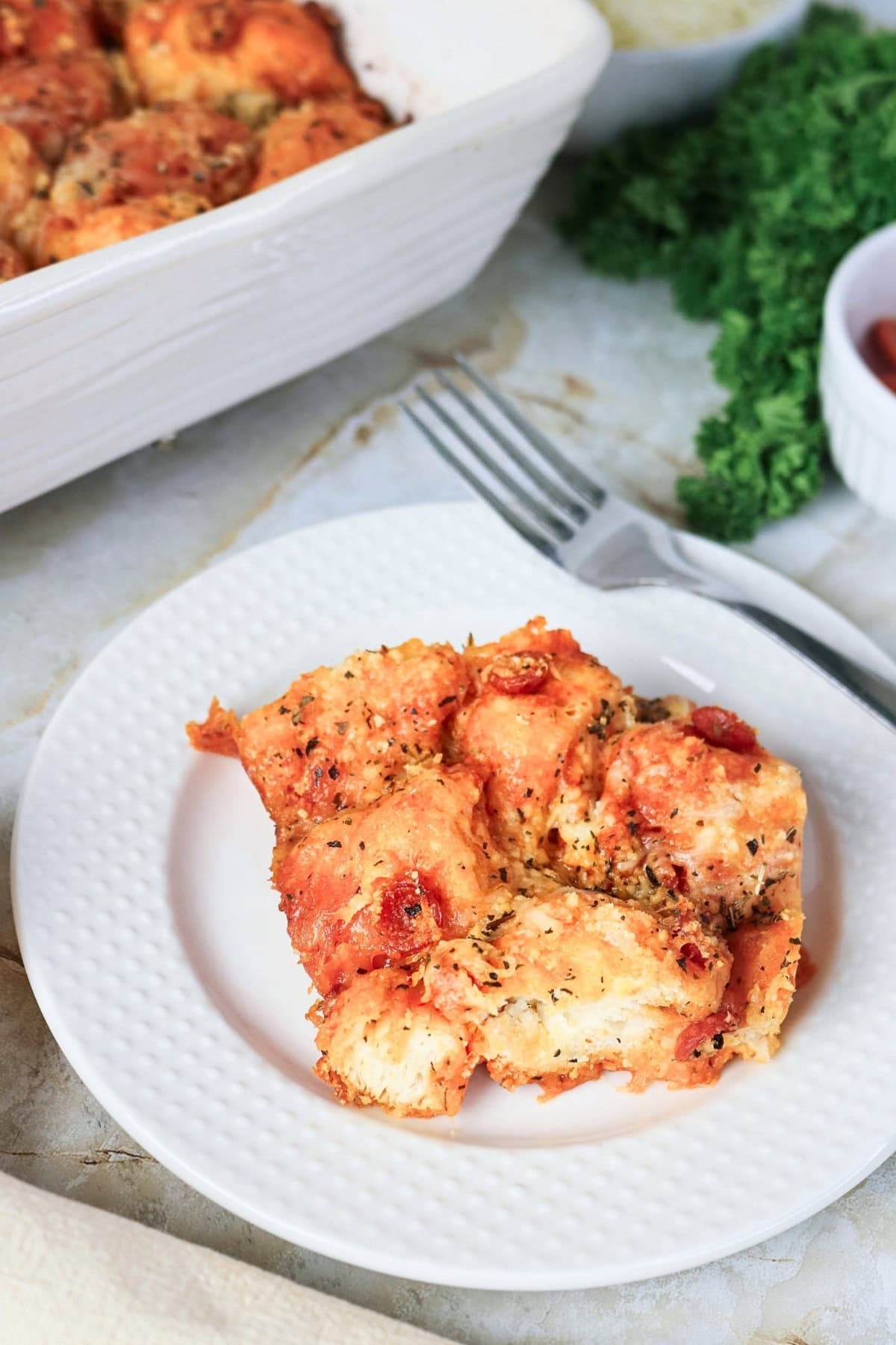 A serving of cheesy pizza monkey bread on a white plate with a fork.
