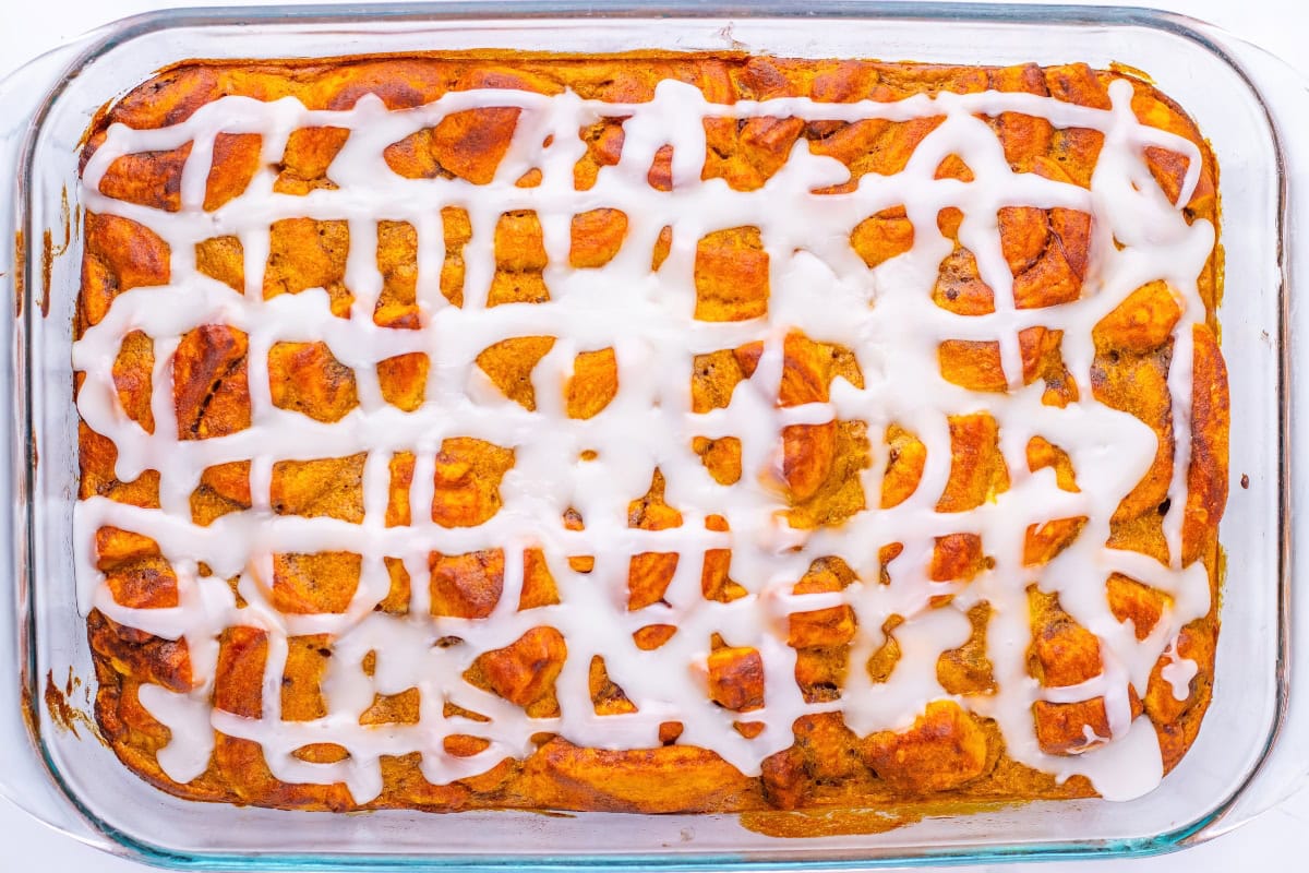 Baked cinnamon roll casserole in a glass dish drizzled with white icing.