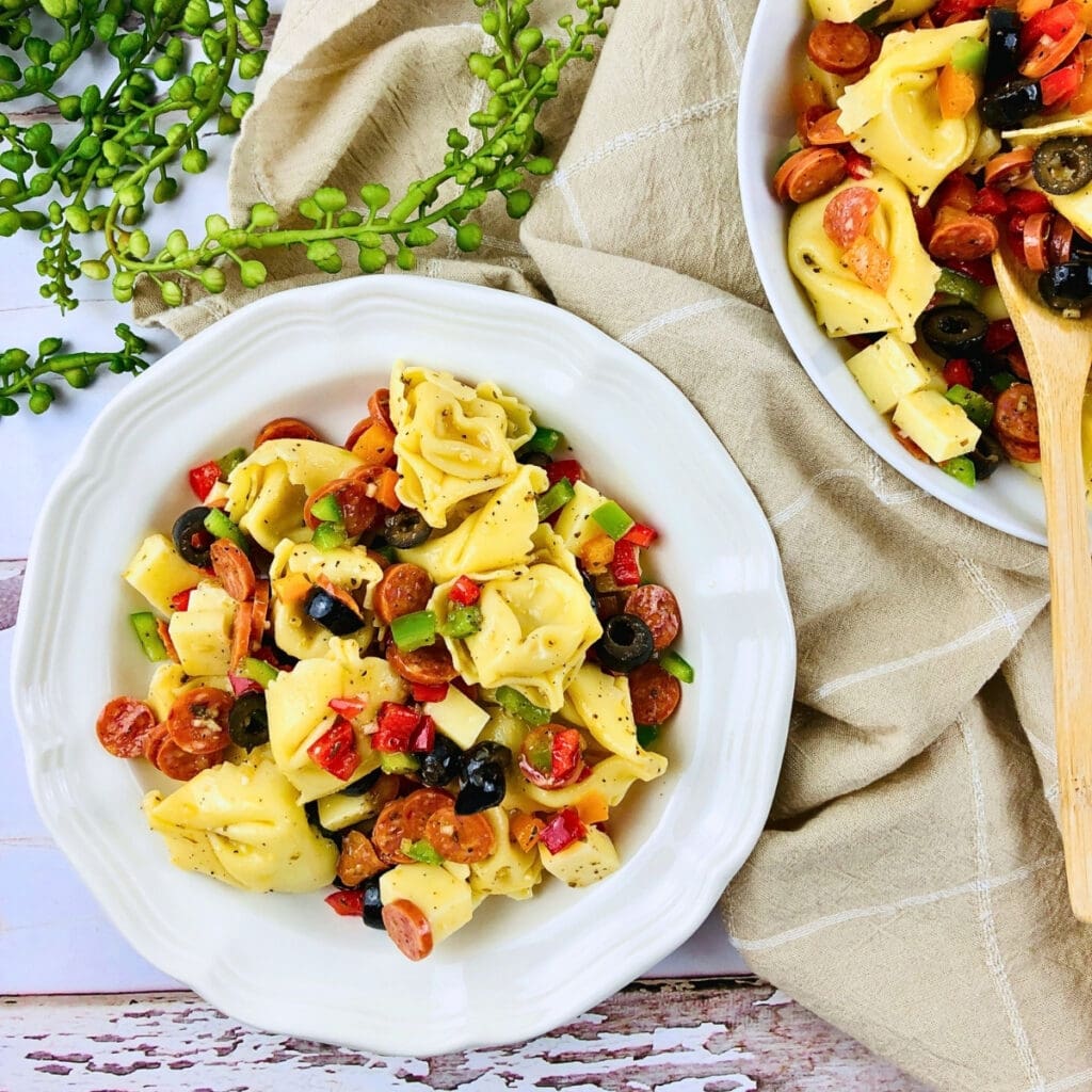 Tortellini pasta salad with veggies and olives in a white bowl on a table.