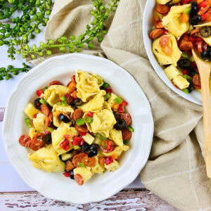 Tortellini pasta salad with veggies and olives in a white bowl on a table.