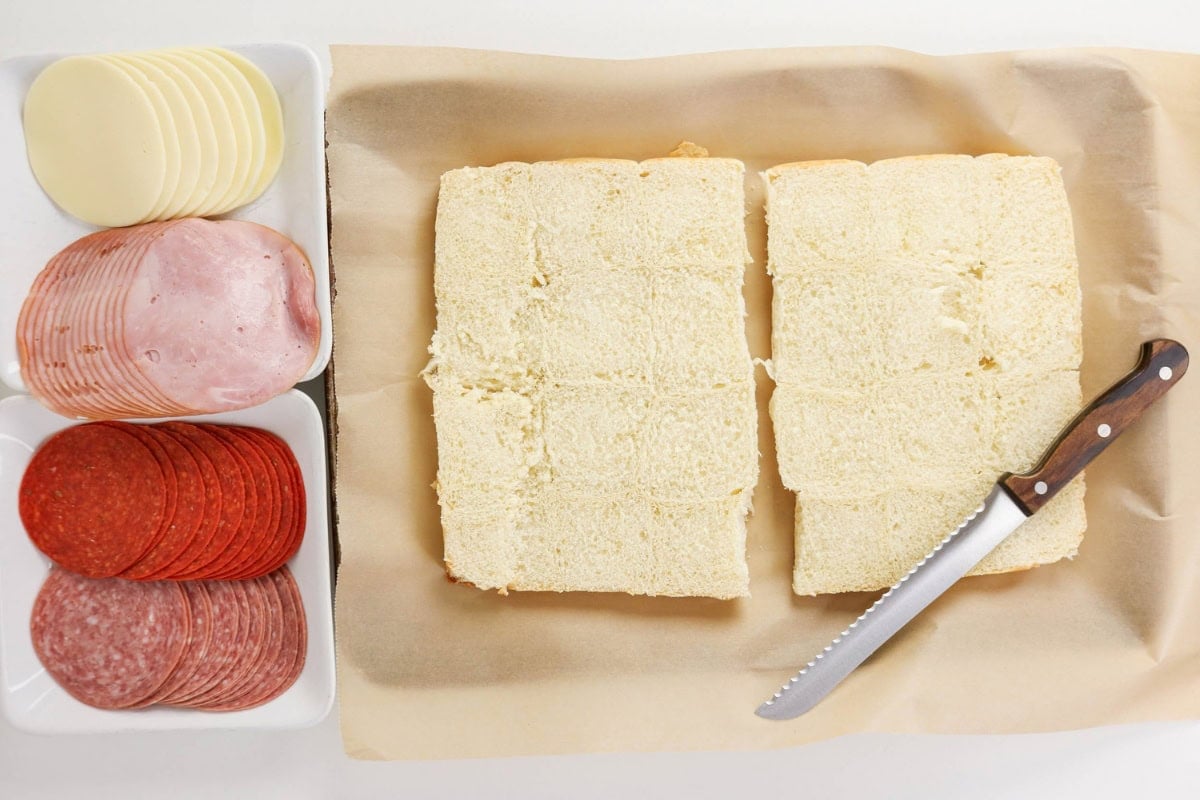 Sliced bread, deli meats, cheese, and a knife on parchment paper.