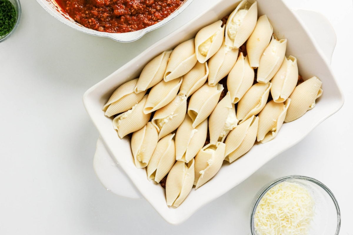 Jumbo pasta shells stuffed with cheese in a baking dish next to meat sauce.