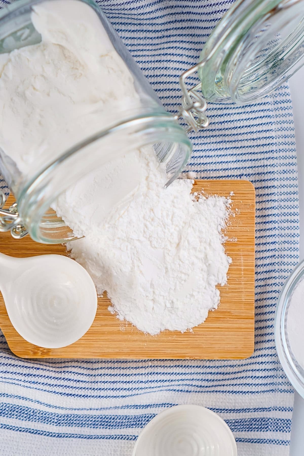Baking powder spilled from a glass jar onto a wooden cutting board.