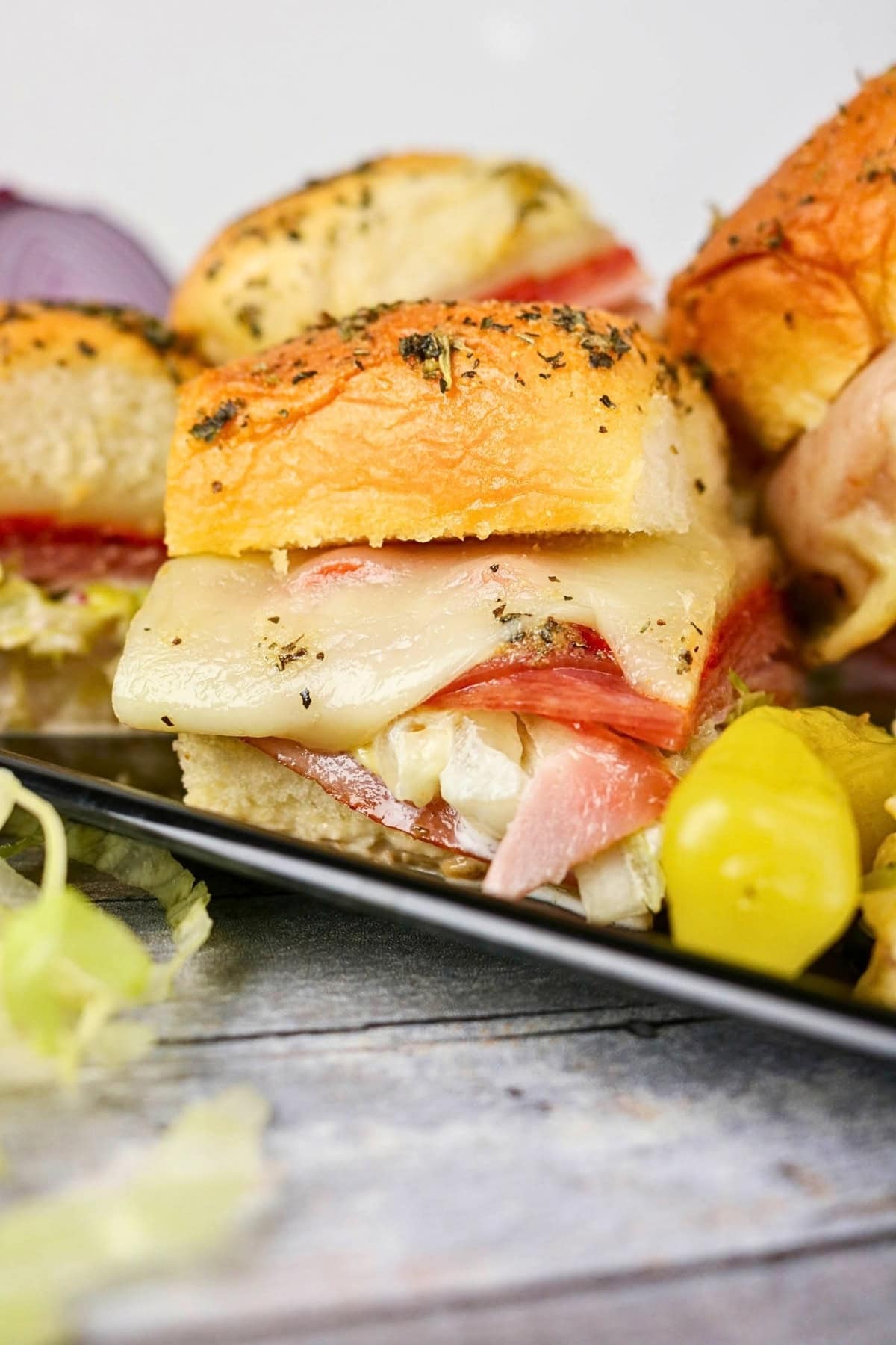 Mini sandwich with melted cheese, lettuce, ham, and a pepper on the side.