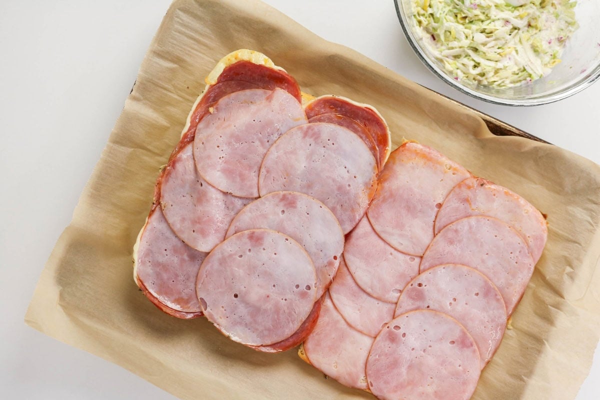Sliced deli meats layered on parchment paper next to a bowl of salad mixture.