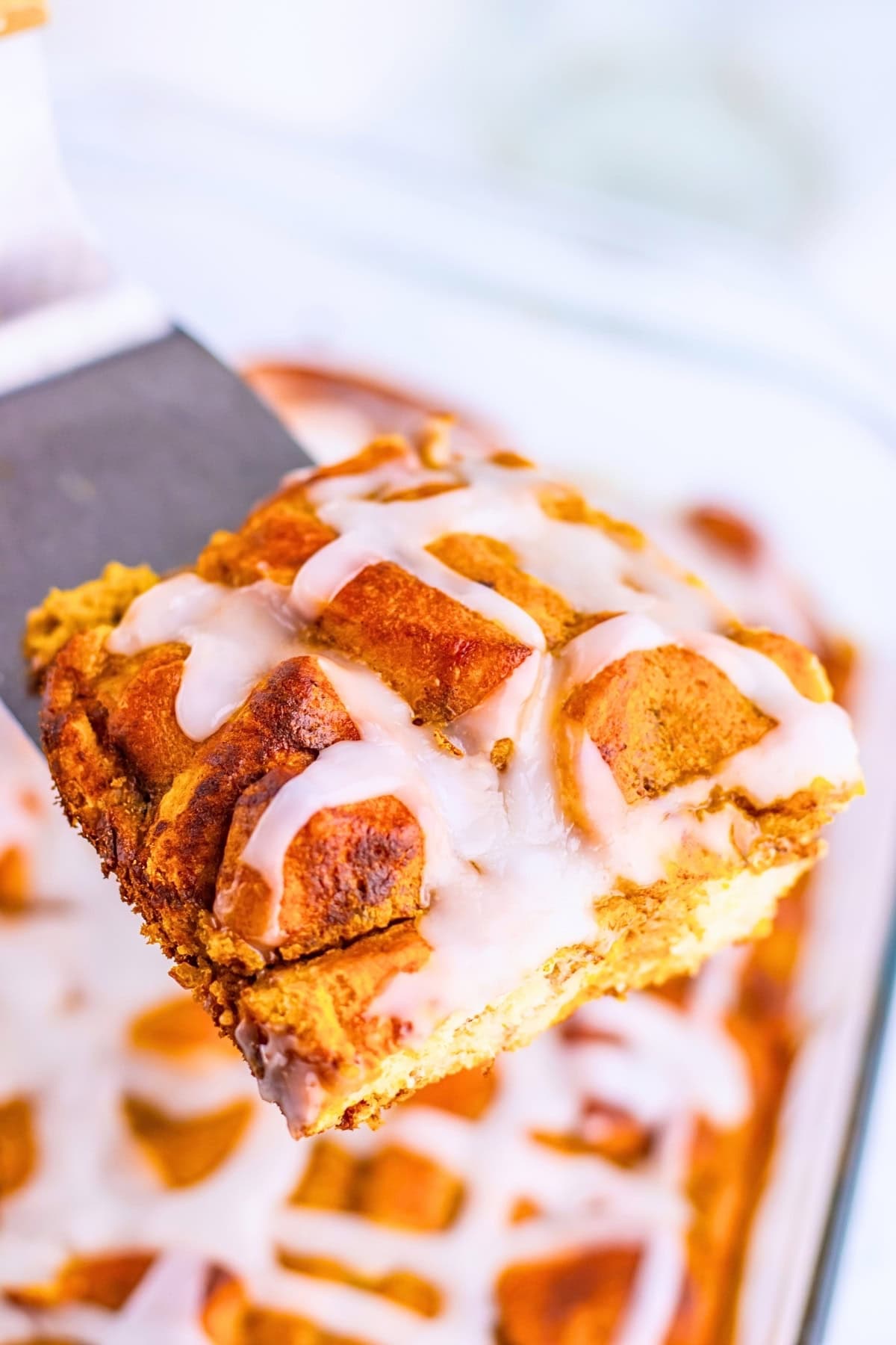 A spatula lifting a square of glazed cinnamon roll bread pudding.