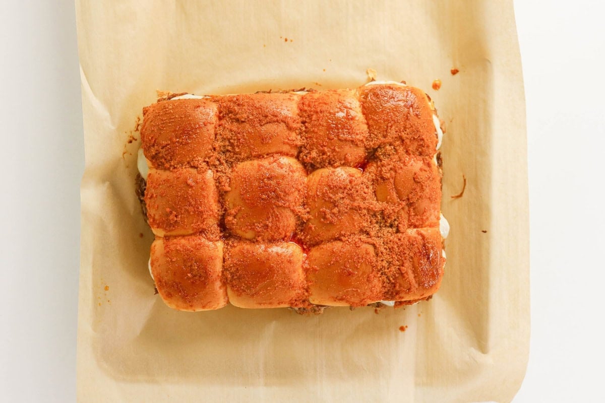 A baked pull-apart sandwich with a golden, seasoned top on parchment paper.