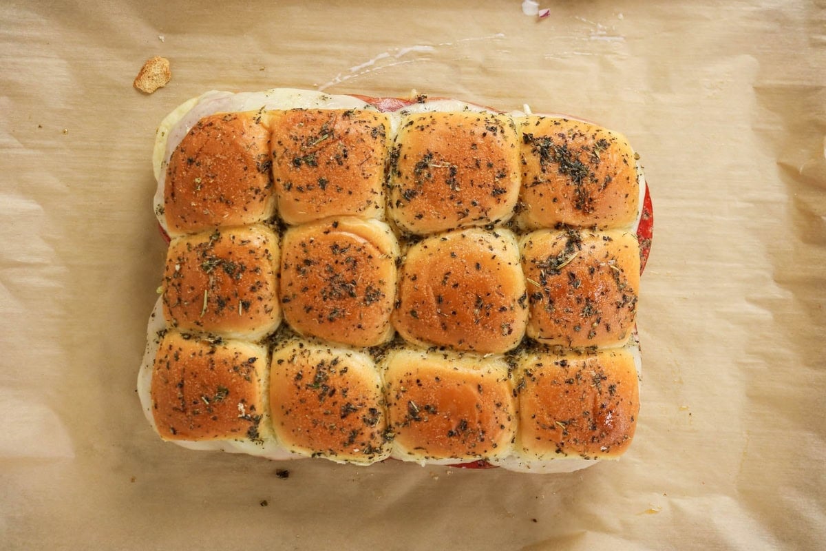 Twelve seasoned sandwich slider buns on parchment paper.