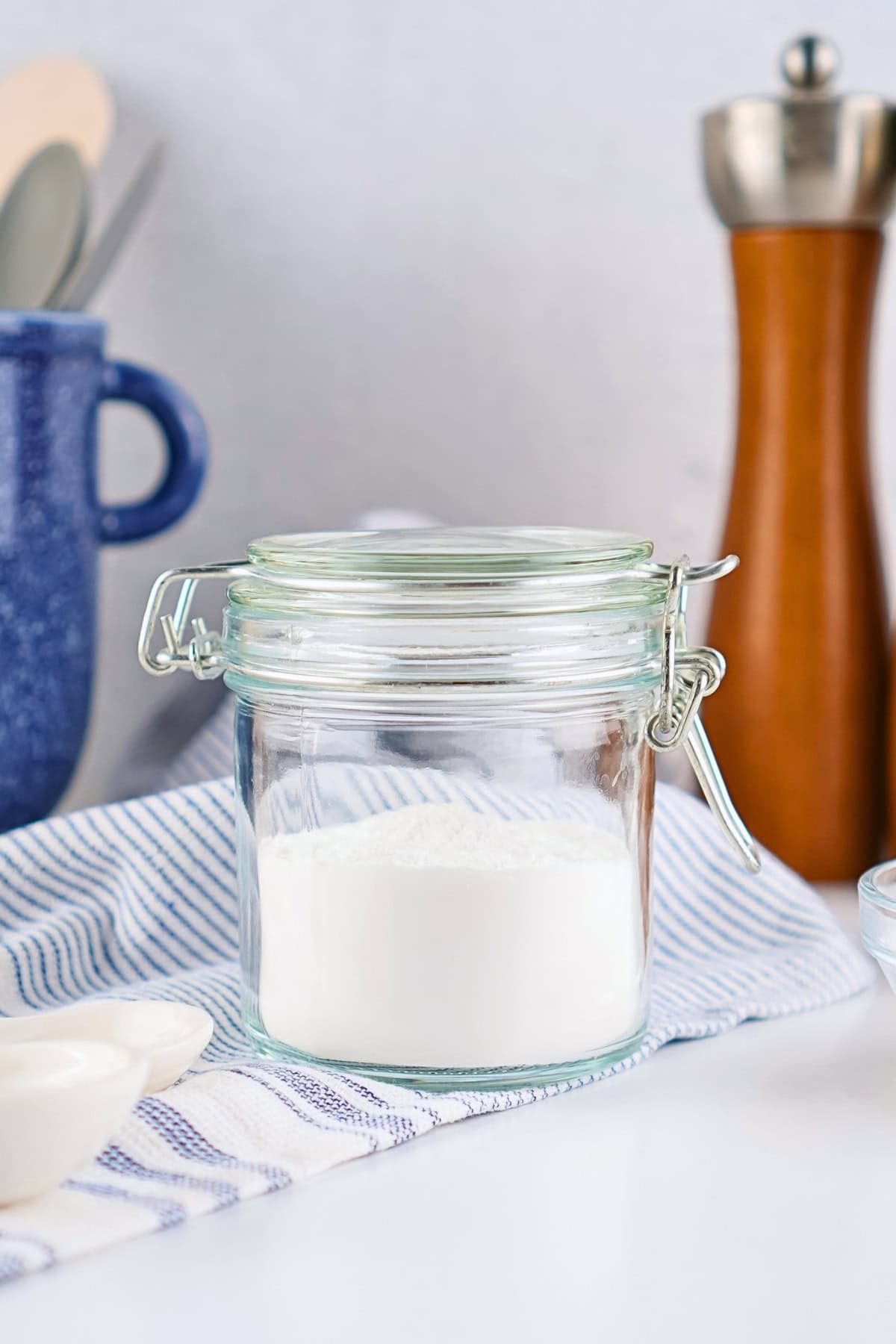 A glass jar filled with flour on a blue and white striped cloth.