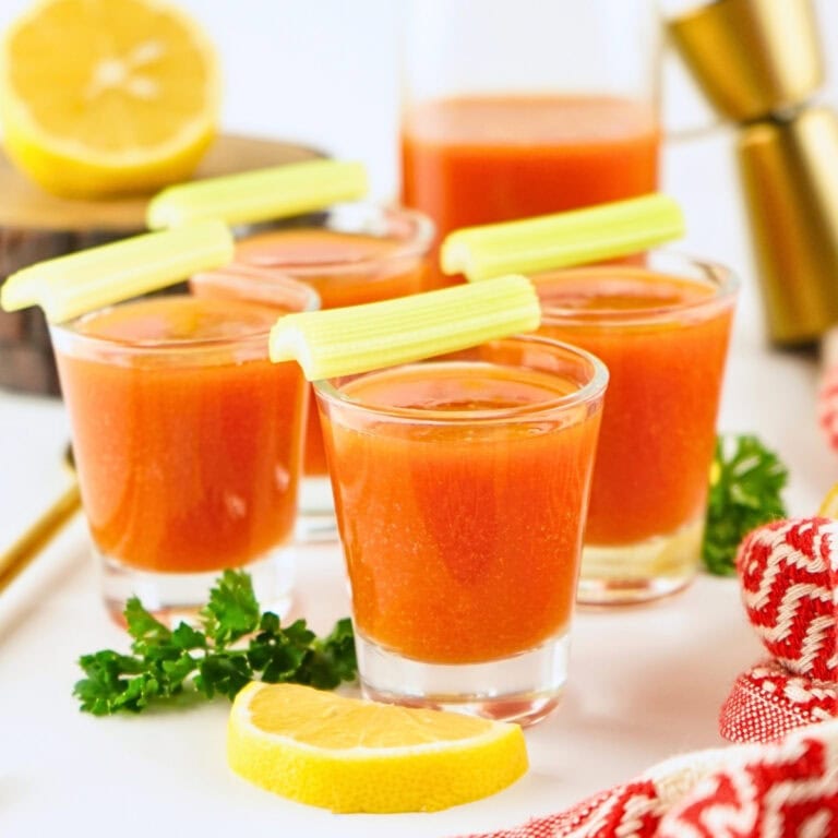 Small glasses of orange cocktail garnished with celery stalks and lemon slices.
