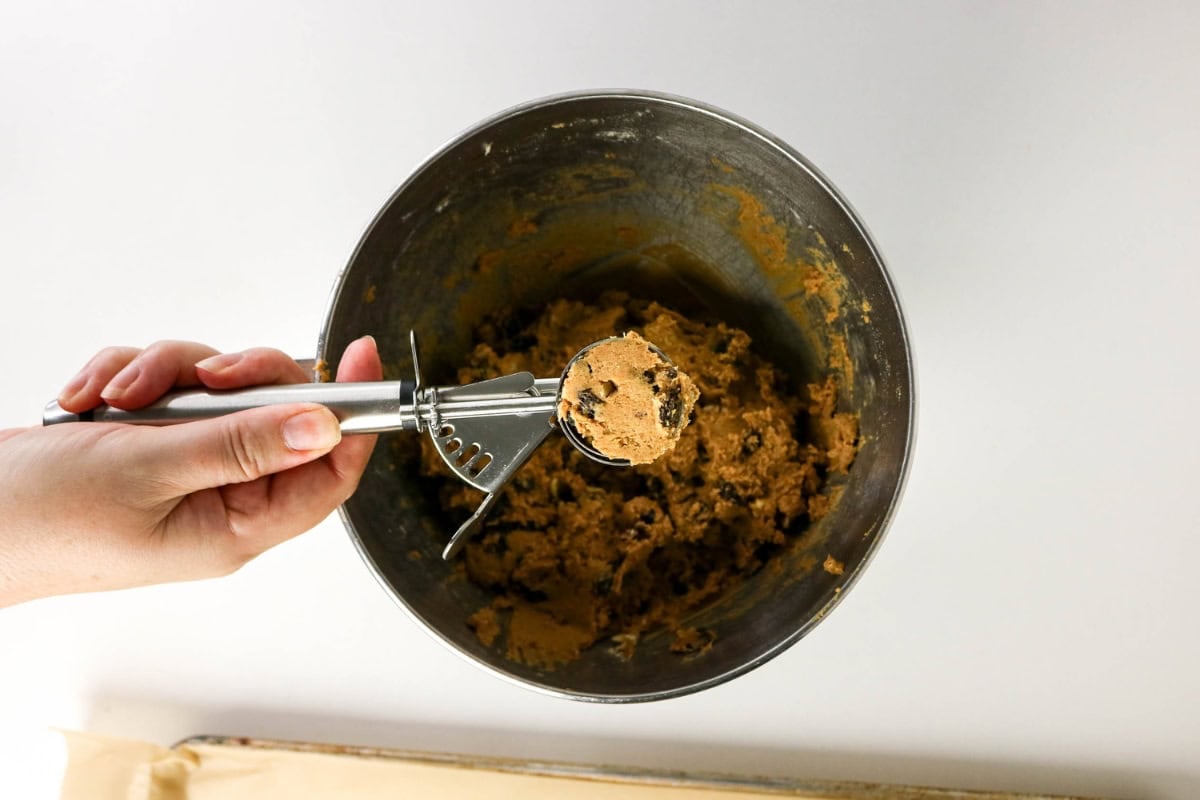 Hand holding a cookie scoop filled with dough over a mixing bowl.