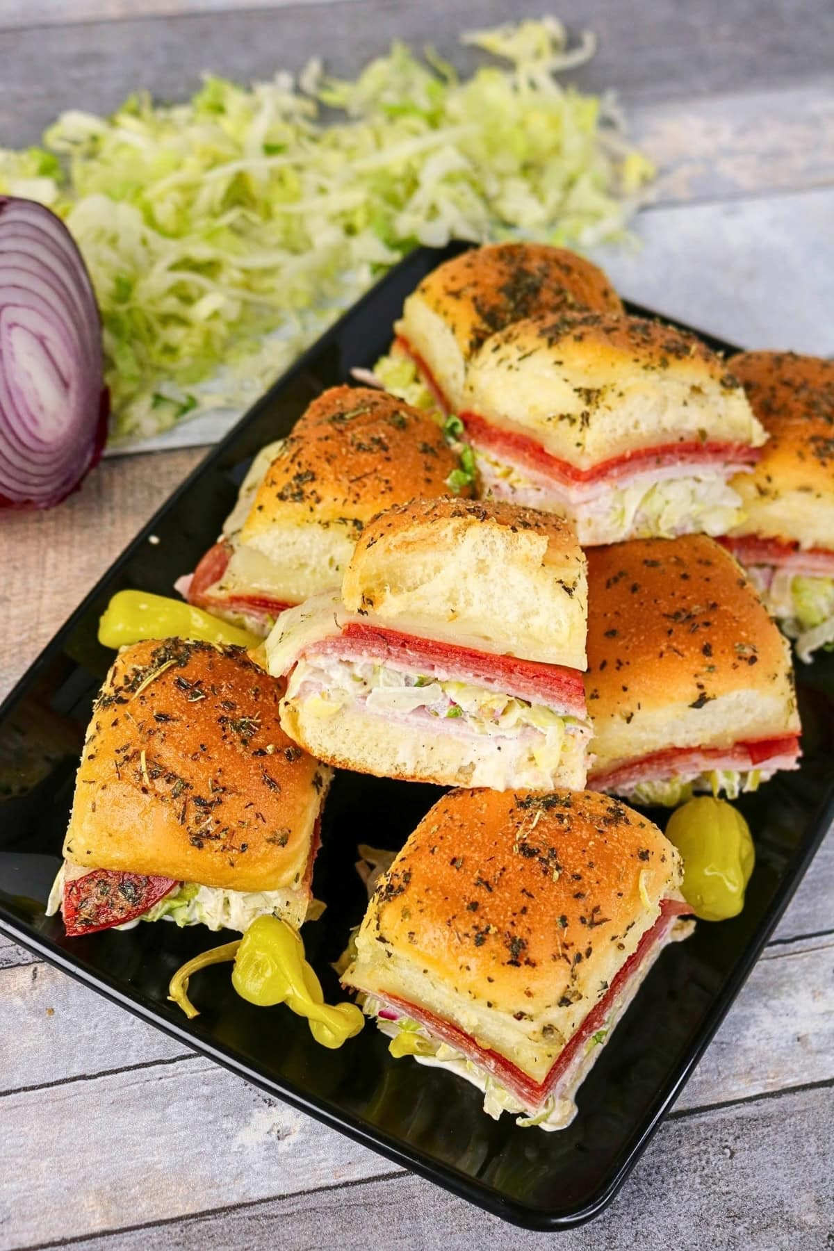 A plate of deli meat sliders with Italian seasoning on slider buns.