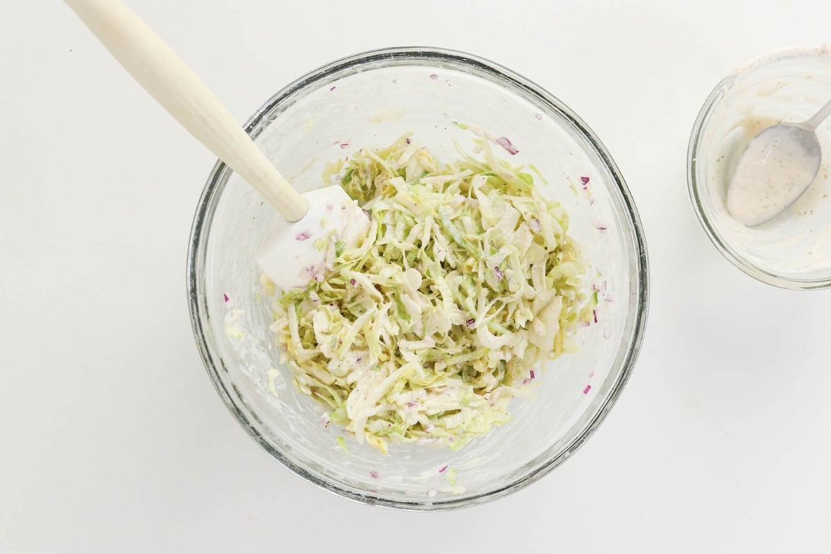 A glass bowl of coleslaw with a spatula on a white surface.