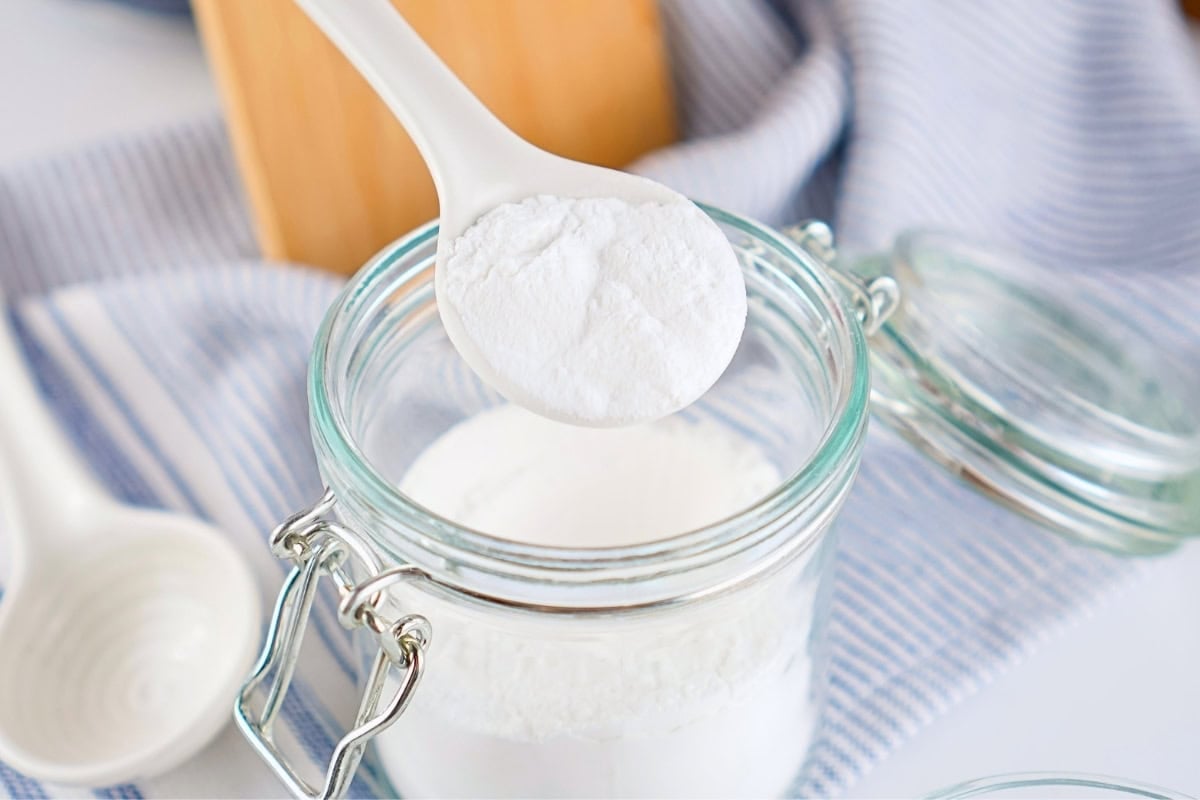 A white spoon holding white powder over an open glass jar.
