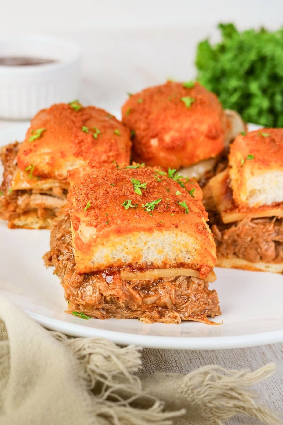 BBQ pulled pork sliders topped with parsley on a white plate.