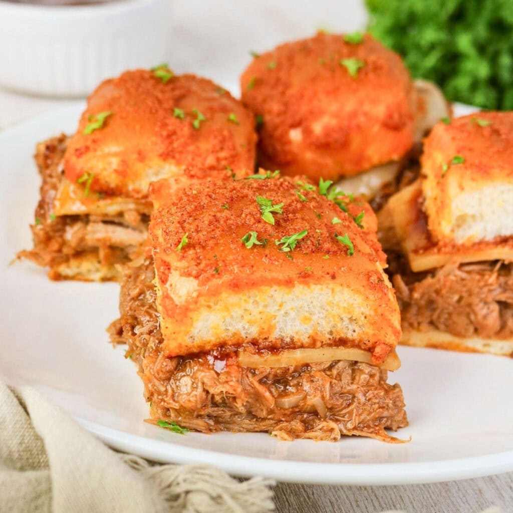 Pulled beef sliders with melted cheese and herbs on a white plate.