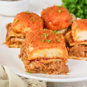 Pulled beef sliders with melted cheese and herbs on a white plate.