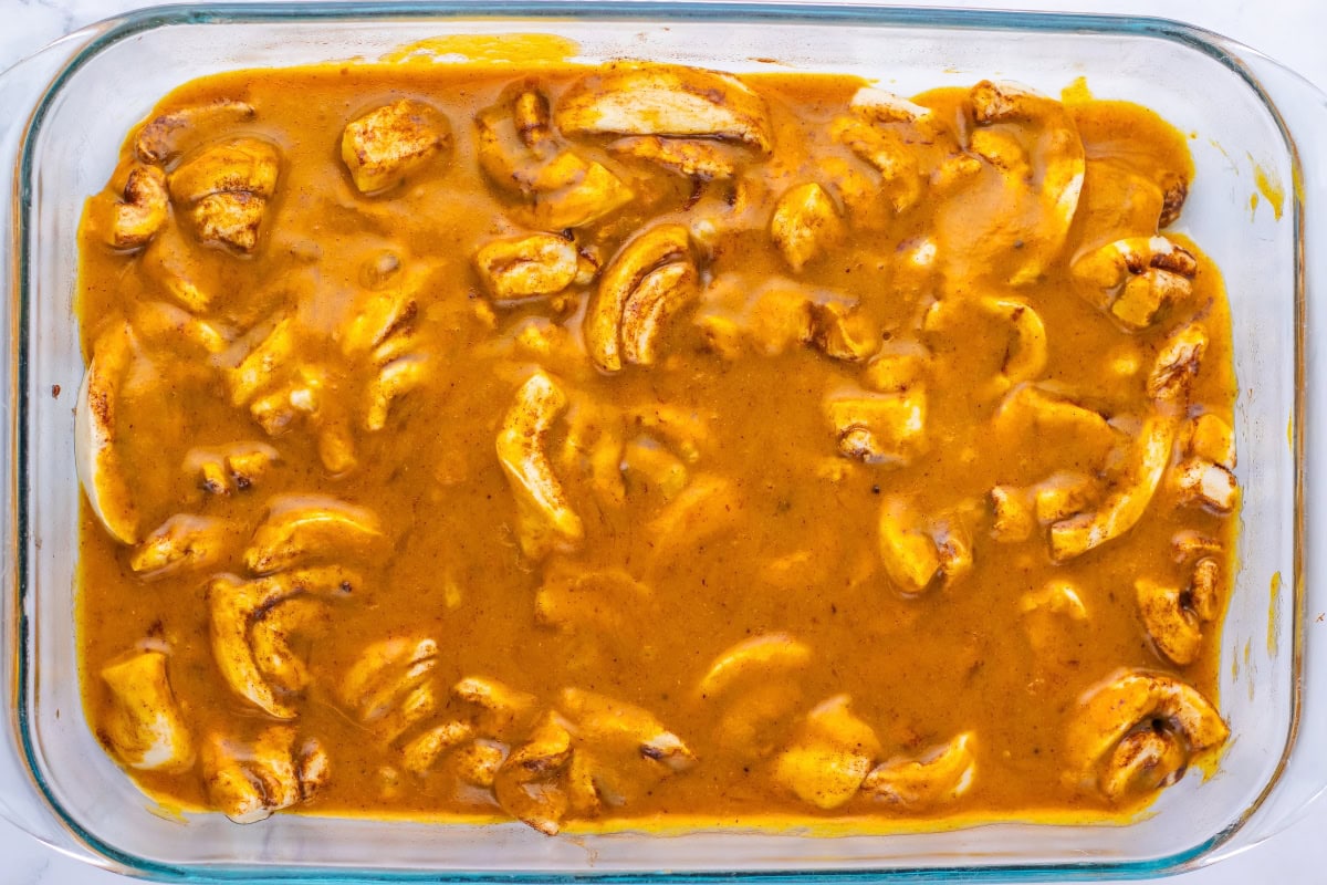 Chunks of chicken in a yellow curry sauce inside a glass baking dish.