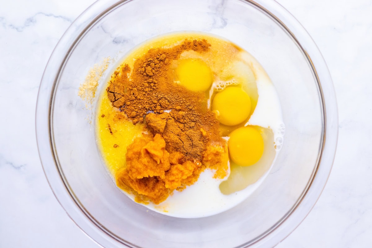 A glass bowl containing eggs, milk, pumpkin purée, and spices.