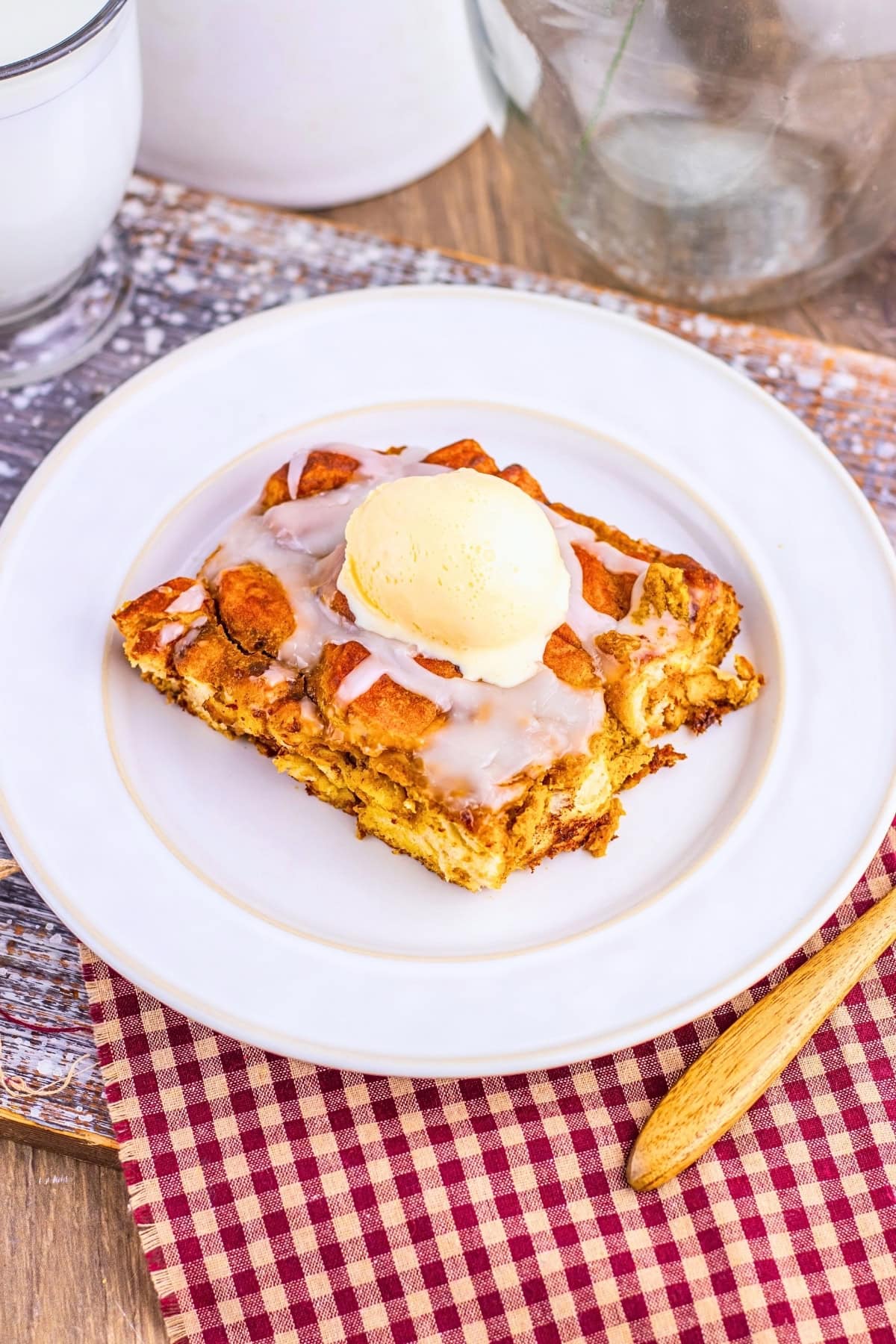 A square slice of bread pudding topped with icing and a scoop of ice cream.