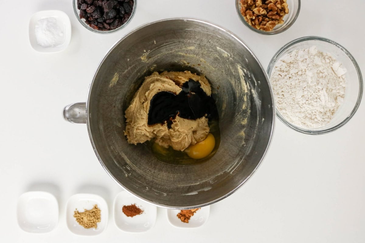 Mixing bowl with cookie dough, an egg, and molasses, surrounded by ingredients.