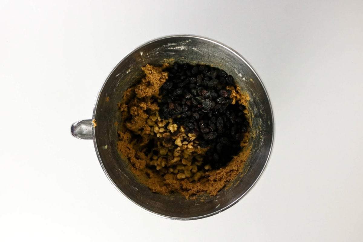 Mixing bowl filled with cookie dough, raisins, and chopped nuts.