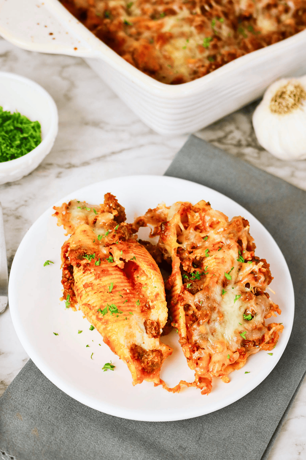 Two stuffed pasta shells topped with melted cheese on a white plate.